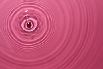 Rippled surface of clear water on bright pink background, top view