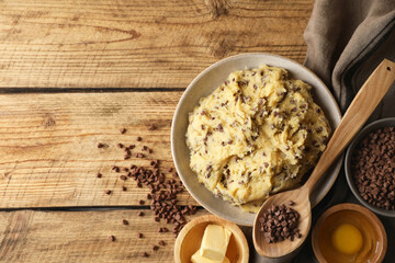 Chocolate chip cookie dough in bowl and ingredients on wooden table, flat lay. Space for text