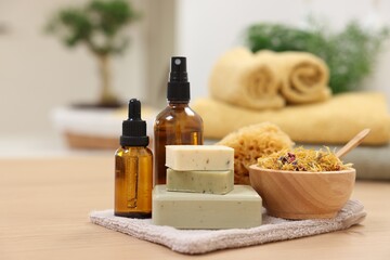 Bottles of essential oils, bowl with dry flowers, soap bars and natural sponge on light wooden table. Spa therapy