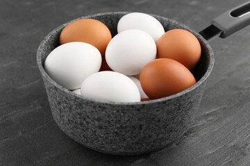 Unpeeled boiled eggs in saucepan on dark grey table, closeup