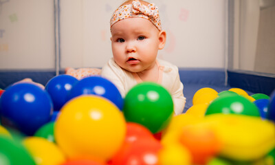 Fototapeta na wymiar Cute baby girl playing with colorful balls in kindergarten.