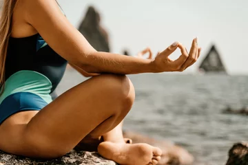Schilderijen op glas Yoga on the beach. A happy woman meditating in a yoga pose on the beach, surrounded by the ocean and rock mountains, promoting a healthy lifestyle outdoors in nature, and inspiring fitness concept. © svetograph