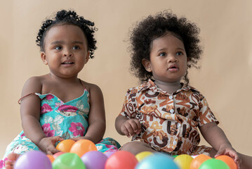 Two Nigerian girls, ages 2 and 1, have beautiful curly hairstyles on a colored background. Sit on...