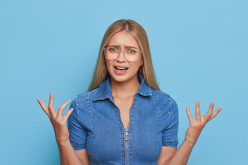 Long-haired pretty girl in glasses standing isolated holding hands up with very annoyed expression on her face, irritation concept, copy space