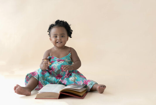 A 2-year-old Nigerian baby girl with beautiful curly hair, sitting on the floor, holding a yellow crayon and looking up. African baby and enhancing the development of children by studying art concept.
