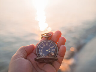 Close up of vintage pocket watch in woman hand with sea in the sunset time as background.