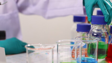 laboratory setting with colorful liquids in test tubes and a person wearing a lab coat and gloves.