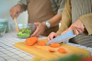 Senior woman chopping carrot on wooden board for salad. Healthy eating concept.