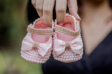 Sapatinho de bebe rosa para menina na mão da mae com vestido preto. Não aparece o rosto da mae.