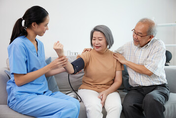 caregiver or nurse measure blood pressure to senior woman on sofa