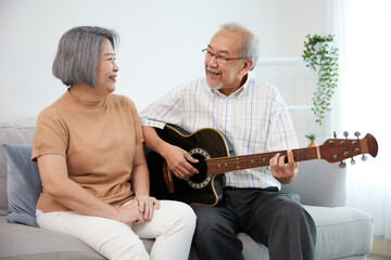 senior couple playing acoustic guitar together on sofa