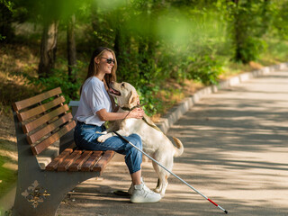 Blind young woman cuddling with guide dog while sitting on a bench. 