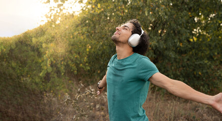 young Arab guy with headphones in wet t-shirt enjoys refreshing summer rain, radiating happiness...