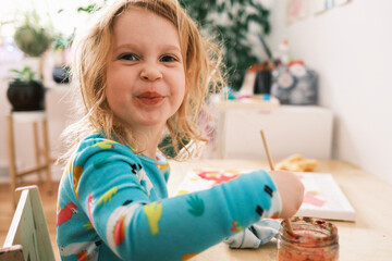 Happy child painting and smiling at the camera - obrazy, fototapety, plakaty