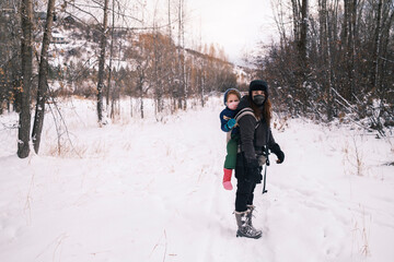 A woman carrying a child in a winter forest hike