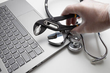 Hand with spanner and stethoscope on laptop, closeup. Concept of