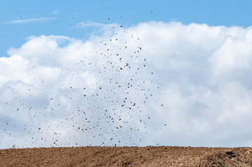 Debris fly after motocross roaring against cloudy sky.