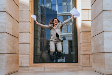Exuberant businesswoman jumps in the air, papers flying, in a display of joy in a modern office...