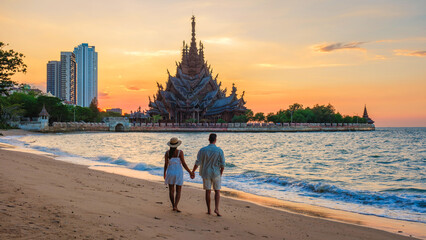 A diverse multiethnic couple of European men and Asian women visit The Sanctuary of Truth wooden temple in Pattaya Thailand at sunset - obrazy, fototapety, plakaty