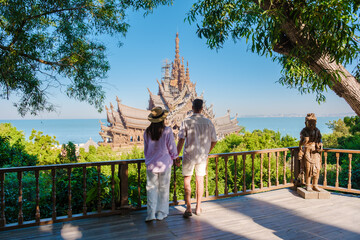 A diverse multiethnic couple of men and women visit The Sanctuary of Truth wooden temple in Pattaya Thailand on a sunny day - obrazy, fototapety, plakaty