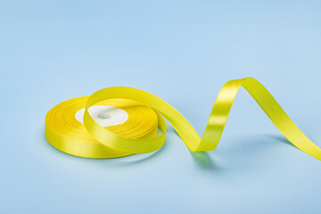 A roll of yellow satin ribbon for gift wrapping. Studio shot, blue background.
