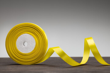 A roll of yellow satin ribbon for gift wrapping. Studio shot, gray background.