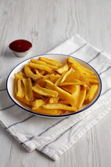 Homemade French Fries with Ketchup on a white wooden background, side view. Copy space.