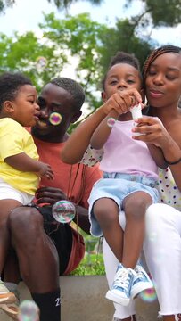 African black ethnicity family with children in playground having fun blowing soap bubbles next to trees in the park