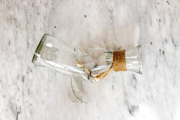A transparent glass bottle shattered into pieces on a marble floor