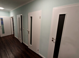 interior painting of the corridor is light blue. white painted doors to rooms and vinyl flooring. laminated plastic has a white strip around the walls. the ceiling is also white