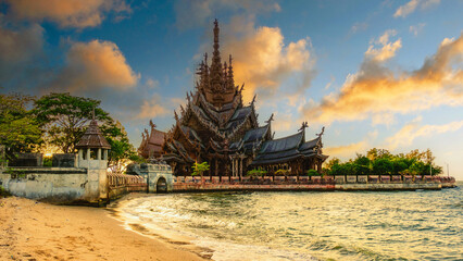 The Sanctuary of Truth wooden temple in Pattaya Thailand is a gigantic wooden construction located at the cape of Naklua Pattaya City Chonburi Thailand at sunset from the beach - obrazy, fototapety, plakaty