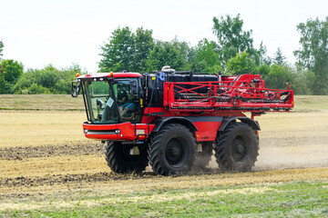 A new modern crop sprayer in the transport condition drives over a field of harvested crop