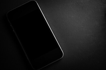Smartphone with blank screen on black background. View from above.