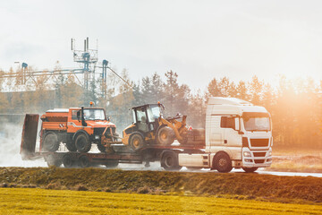 Heavy-duty truck hauls heavy construction equipment and trucks on a trailer. Amidst a dusty...
