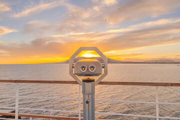 Jumelles sur le pont d'un navire de croisière en navigation en mer avec un coucher de soleil.	