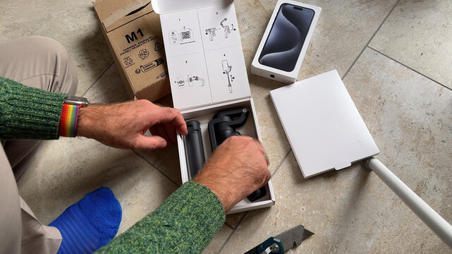 Paris, France - Jun 10, 2023: POV overhead view of a male hand unboxing the new DJI Osmo Mobile 6 smartphone stabilizer from its cardboard packaging