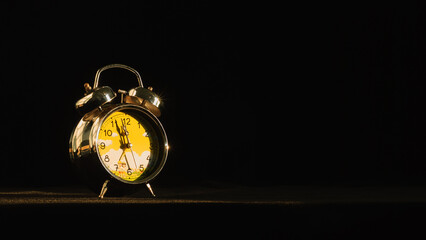 Merry Christmas and Happy New Year concept. Silver alarm clock on table with evening sunlight on black background. Countdown to New Year's Eve ready to welcome the new year. 2024. Free space for text. - obrazy, fototapety, plakaty