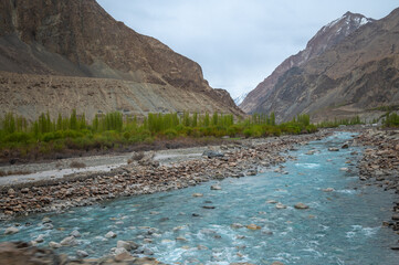 A river stream flows through a mountain landscape. Image of Shyok river in Turtuk, Ladakh