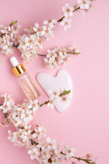 Glass bottle with oil, Gua sha stone for face massage on a pink background with blooming cherry....