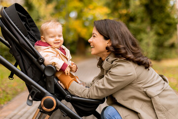 Young woman with cute baby girl in baby stroller at the autumn park