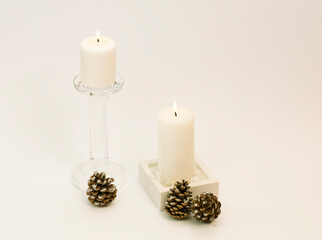 Winter composition – lit, white candle in glass candle-holder and silver decoration in glass vase. White background. 