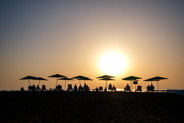 Fototapeta na wymiar Silhouette of peoples and beach umbrella at the sunset in the sea