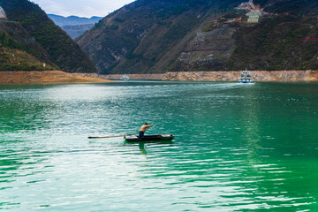 The sun sets and the mountains surround the Yangtze River. The water is dark blue and the sky is colorful. The mountain is reflected in the water.