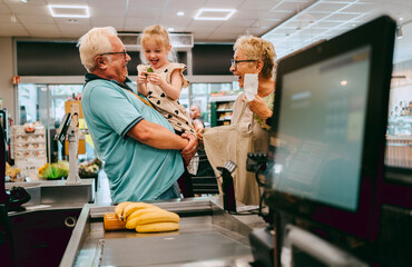 Happy granddaughter having fun with grandparents while shopping at supermarket