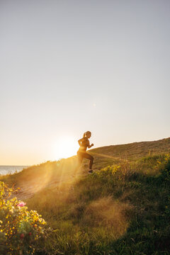 Side view of mature woman jogging on hill against sky at sunset