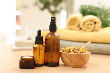 Bottles of essential oils, dry flowers and jar with cream on light wooden table. Spa therapy