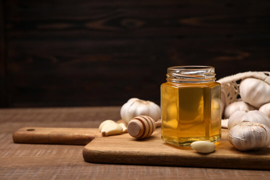 Jar with honey, garlic and dipper on wooden table, space for text