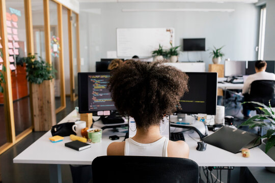 Rear view of female computer programmer sitting at desk in office