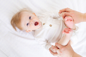 close-up portrait of a baby 6 months old, a blond boy with blue eyes yawns on a white bed in a...