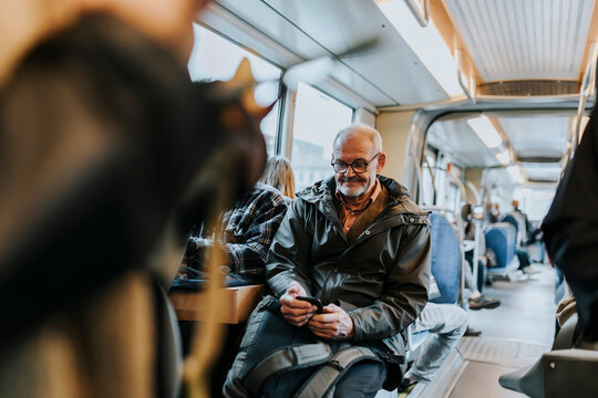 Elderly man using smart phone and sitting in bus while traveling to work